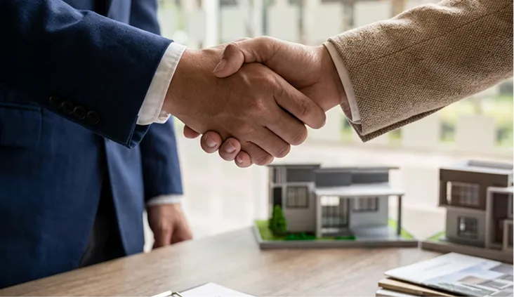 Apreton de manos en una reunion inmobiliaria con maquetas de casas