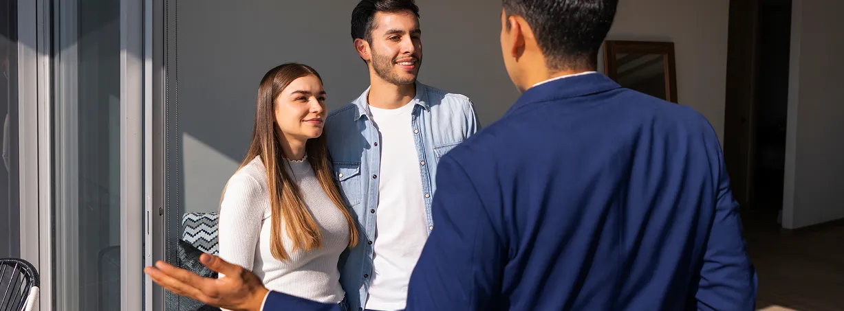 Asesor inmobiliario conversando con una pareja junto a una ventana